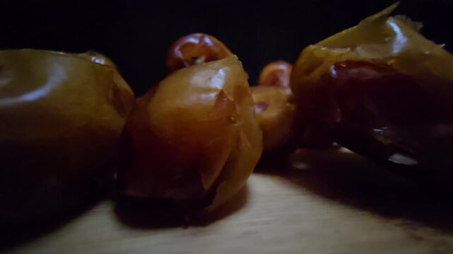 A high-quality, close-up shot of premium Saudi Khalas dates with a glossy golden-brown texture and thin skin, elegantly arranged on a rustic wooden board against a moody dark background, highlighting 