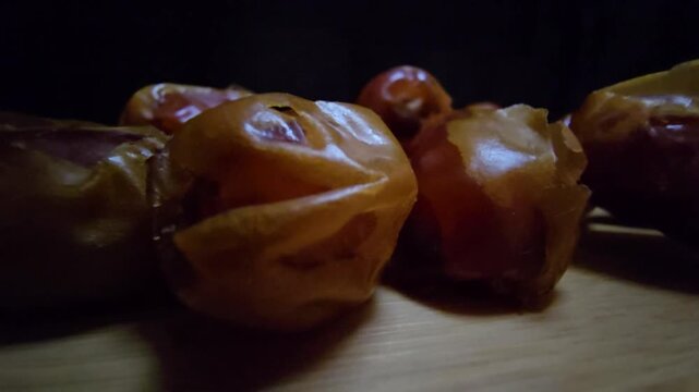 A high-quality, close-up shot of premium Saudi Khalas dates with a glossy golden-brown texture and thin skin, elegantly arranged on a rustic wooden board against a moody dark background, highlighting 