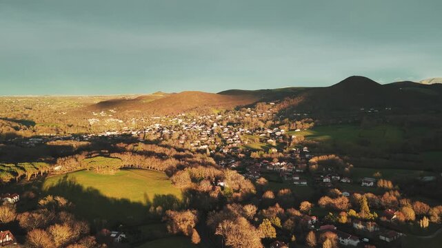 Aerial view of Ascain showcasing a picturesque landscape with hills and houses nestled among the trees casting long shadows in the afternoon sun, Ascain, Nouvelle-Aquitaine, France.