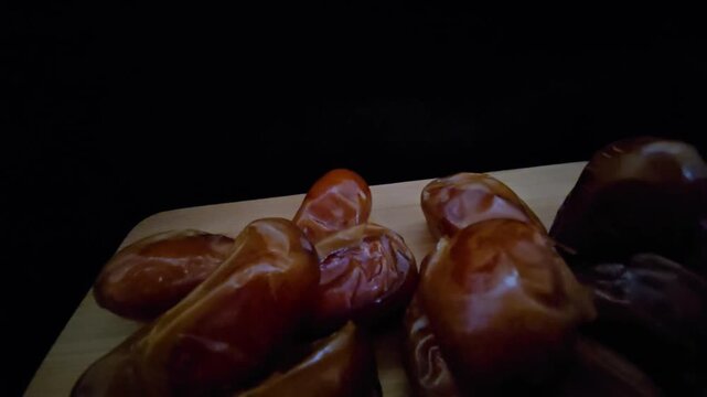 A high-quality, close-up shot of premium Saudi Khalas dates with a glossy golden-brown texture and thin skin, elegantly arranged on a rustic wooden board against a moody dark background, highlighting 