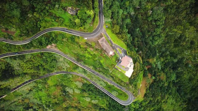 Aerial top down view of a car driving on a winding serpentine mountain road near Lombo do Pico, drone tracking sideways over hairpin bend and lush green terraces in Madeira island road trip.