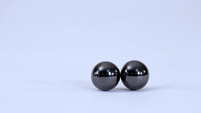 Two Shiny Magnetic Spheres Attracting and Connecting on a White Surface