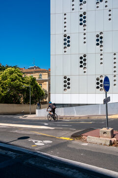Modern building facade architecture beside street sidewalk as cyclist passes under shadow creating pattern against clear blue sky
