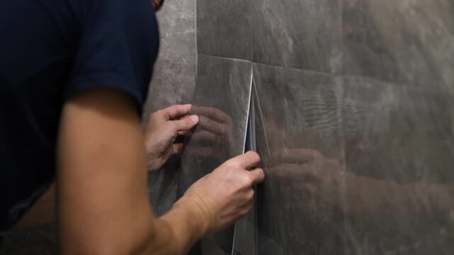 A man glues wall panels onto old tiles. A quick and affordable renovation