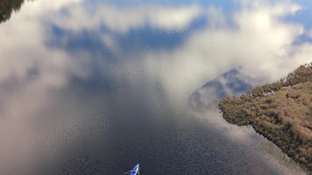 Aerial view of a lone kayaker cutting through the still, dark waters next to a shoreline, reflecting the cloudy sky, Callander, Scotland, United Kingdom.