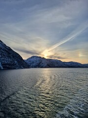 Fototapeta premium Cold northern sea surrounded by snow-covered mountains at winter sunset. Calm Arctic waters and dramatic sky.