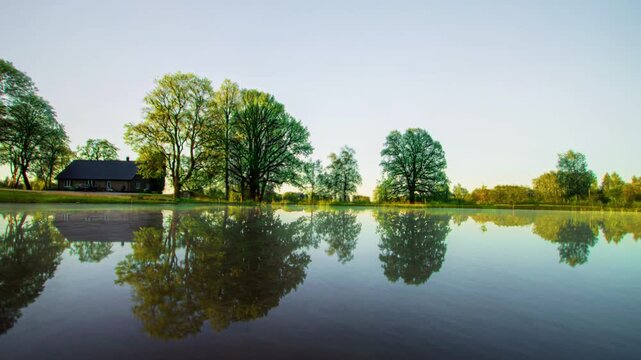 Timelapse over a countryside dam with surrounding trees showing four seasons change, weather transition and climate patterns, global warming and environmental change concept, natural landscape