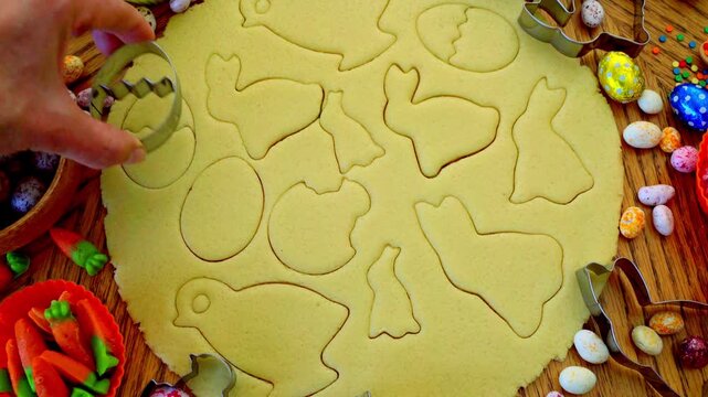 
A woman carves Easter cookies in the shape of bunnies, chickens, and eggs. Preparing for the holiday. Traditional baking.