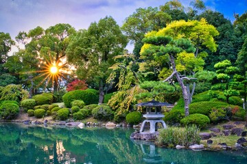 Fototapeta premium Autumn Sunset Flare Through Red Maple Leaves in Osaka Castle Japanese Garden at Main Palace Area