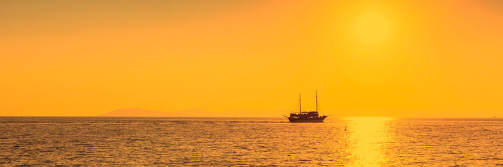 Fototapeta premium Sun setting at the sea with sailing ship