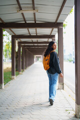 Fototapeta premium Young woman with backpack walking along a covered outdoor pathway, pausing and looking back, conveying concepts of journey, discovery, and urban exploration