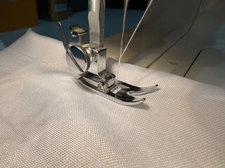 Sewing machine needle and presser foot on white fabric, conceptual close up for textile craft, fashion design, and handmade hobby.