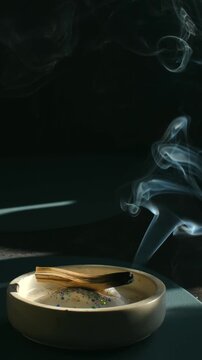 Smoldering palo santo wood releasing fragrant, purifying plume of smoke in ceramic holder for spiritual cleansing ritual, energy clearing, aromatherapy, meditation practice. Palo santo wood burning