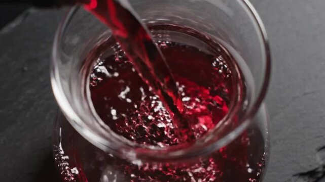 Red wine being poured into a clear glass decanter against a dark backdrop creating beautiful bubbles