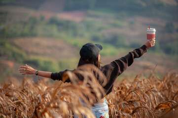 Asian woman standing holding a cup of coffee in a rice field, happy. © Pongsorn