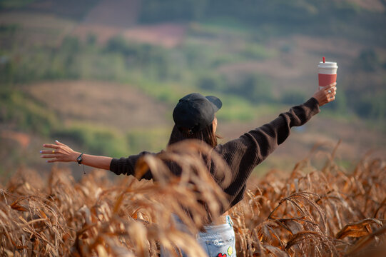Asian woman standing holding a cup of coffee in a rice field, happy.
