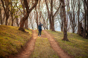A woman stands in the middle of a forest among cherry blossom trees.