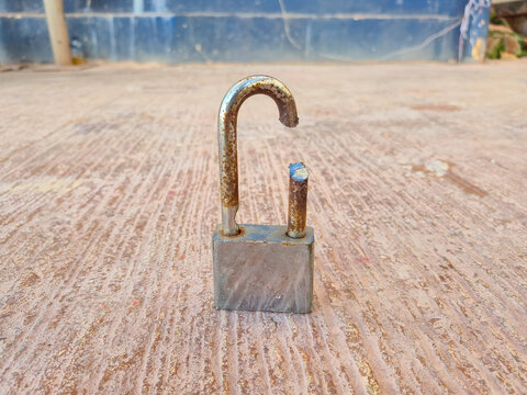 ​Broken silver padlock with a rusted, cut shackle lying on a textured ground. Concept of security breach, burglary, theft, and failed safety protection