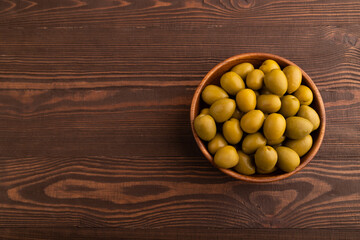 Fresh green olives in wooden bowl on brown wooden. Top view, copy space