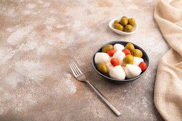 White Mozzarella cheese, with tomatoes and olives on brown concrete, linen textile, side view, copy space.