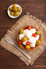 White Mozzarella cheese, with tomatoes and olives on brown wooden, linen textile, top view, close up.