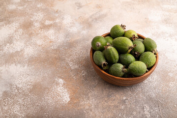 Ripe Feijoa in wooden bowl on brown concrete, side view, copy space