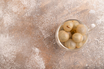 Ripe peeled Longan in glass on brown concrete, top view, flat lay, copy space