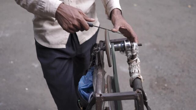 Knife sharpener at work using manual grinding wheel in Mumbai, India.