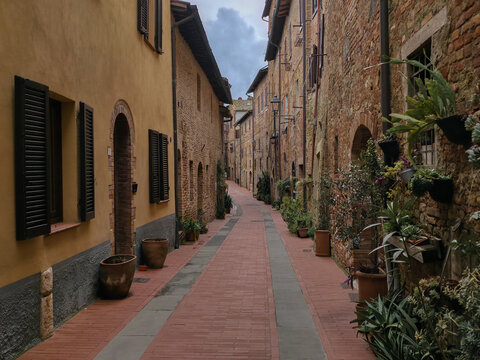 This photo captures the charming, narrow pedestrian main street, Via Alessandro Casolani, within the medieval hill town of Casole d'Elsa, Tuscany, Italy