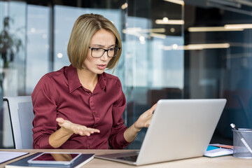 Fototapeta premium Professional woman working in an office facing frustration and confusion with her laptop, gesturing while experiencing a technology problem or technical difficulty