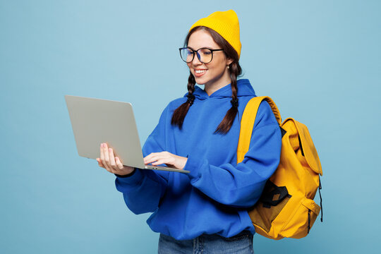 Young smart IT woman student wear casual clothes yellow backpack bag hold use work on laptop pc computer isolated on pastel plain light blue color background. High school college lifestyle concept
