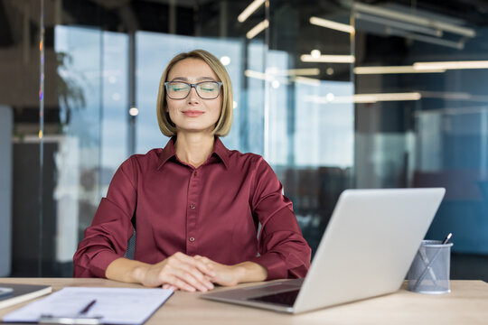 Businesswoman practicing mindfulness and meditation at her office desk, taking a tranquil break from a laptop to improve mental health and reduce workplace stress in a modern corporate environment