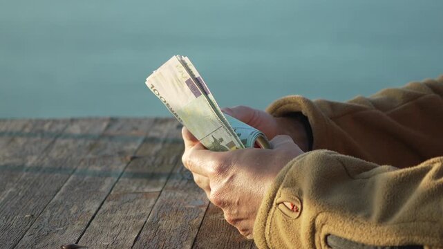 Money, Euro, Counting hands holding large stack of 100 euro banknotes outdoors at golden hour on wooden dock.