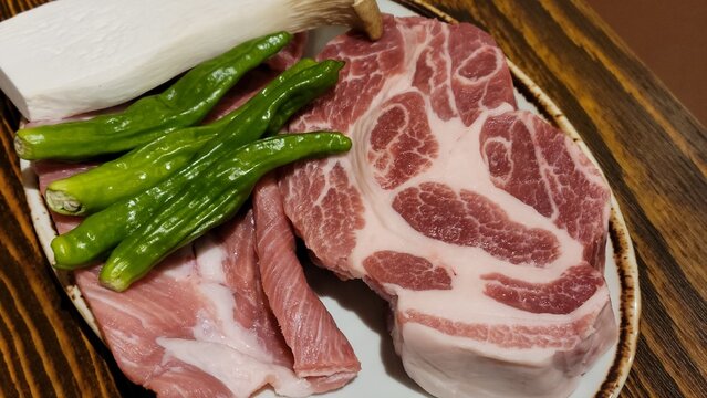 Fresh Raw Pork Neck and Green Peppers Plated on a Table for Barbecue