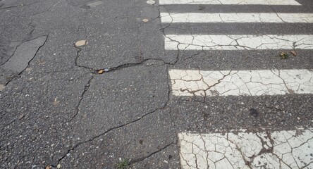 Cracked and uneven pavement surface near faded white pedestrian crossing lines