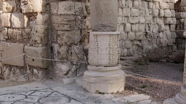 Tilt up footage of ancient carved stone column with detailed relief standing on weathered mosaic floor with geometrical pattern. Roman amphitheatre, Kom el-Dikka archaeological site, Alexandria, Egypt