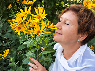 Mature woman enjoys the beauty of yellow flowers during her travel adventure in nature