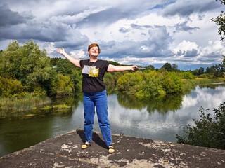 Mature woman joyfully enjoying nature near tranquil lake on a sunny day during her travel adventure