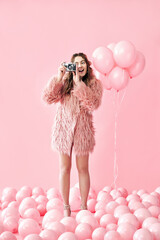 Pretty happy glamour woman taking photo with retro camera over pink background