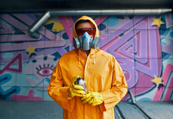Graffiti painter in respirator mask standing near the wall with his paintings