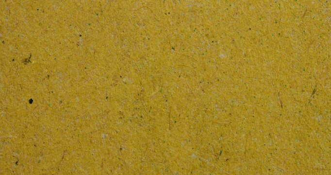 Stop-motion video of warm mustard yellow handmade paper texture with visible fibers and small speckles. Abstract eco-style background for craft, design, and vintage projects.