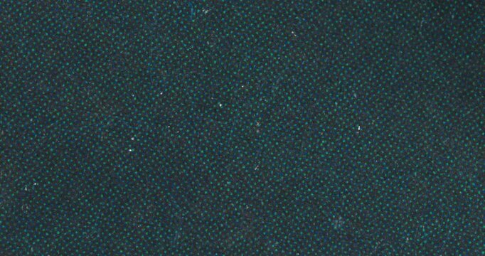 Stop-motion video of dark woven textile with small teal dotted pattern and subtle lint specks. Abstract fabric background for fashion, tech, retro, and design projects.