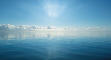 Fototapeta premium Calm sea surface reflecting a radiant blue sky with warm sun rays shining through