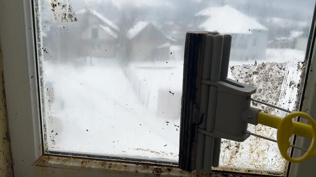 A soldier washes windows in an old barracks, winter and snow-capped mountains outside. The building hasn't been cleaned in years, an abandoned house in the Carpathians.