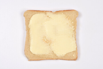 A single square slice of golden toast bread with a thick layer of creamy yellow butter spread on its surface against a plain white background