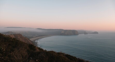 Early light revealing foggy hills and seashore under a calm pastel pink sky
