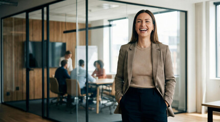 Obraz premium Happy businesswoman in a blazer smiles in a modern office with colleagues have a meeting in a conference room