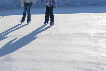 Winter recreation activity. Two skaters-  mother and child on the ice rink in the sunlight. Cold, scratched ice background.