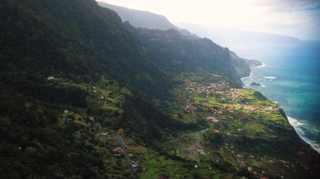 Aerial establishing shot of Arco de Sao Jorge village, drone rising pedestal up revealing massive mountains and Atlantic ocean waves from Beira da Quinta viewpoint in Madeira island, cinematic.