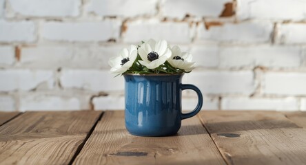 Blue ceramic mug holding fresh white anemones on wooden table in front of textured white brick wall with ample copy space